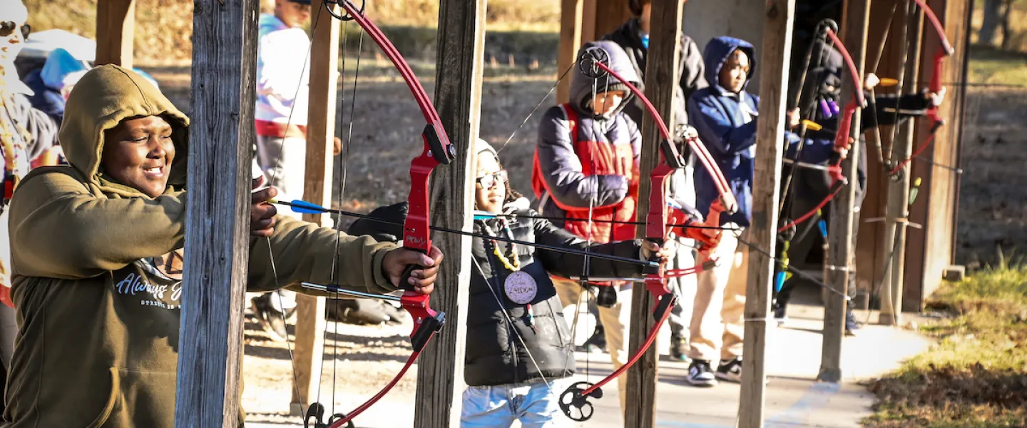Camper aiming a bow at an archery target during a daytime activity
