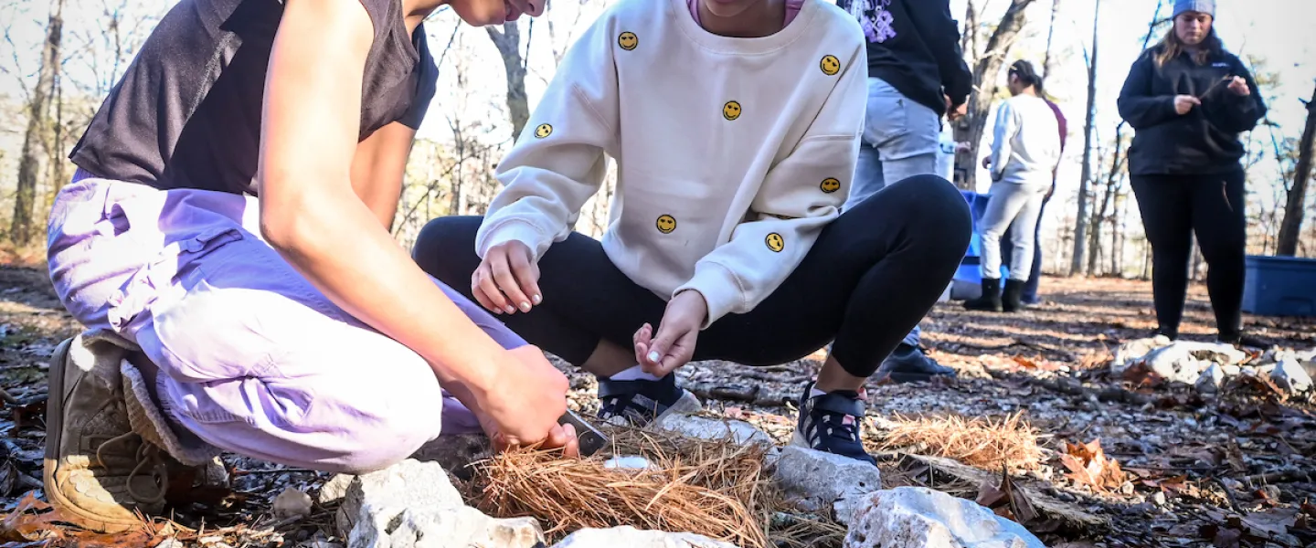 Students working together to start a campfire with sticks and kindling