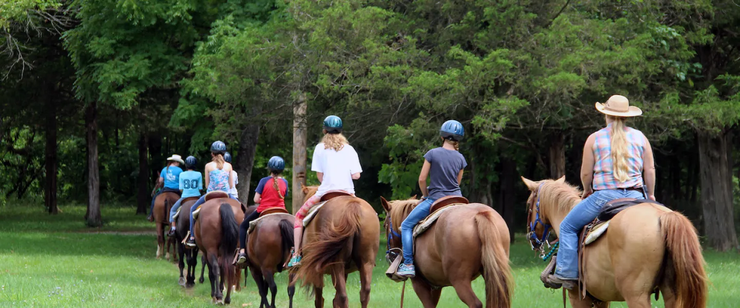 Guests riding horses along wooded trails at YMCA Trout Lodge