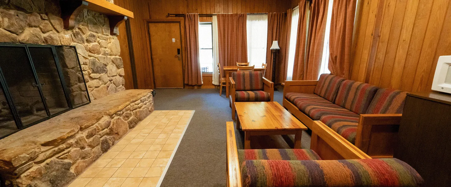 A Lake View Cabin at YCMA Trout Lodge living room space featuring a seating area with couch, chairs, and a coffee table, stone fireplace, mini fridge, and microwave.