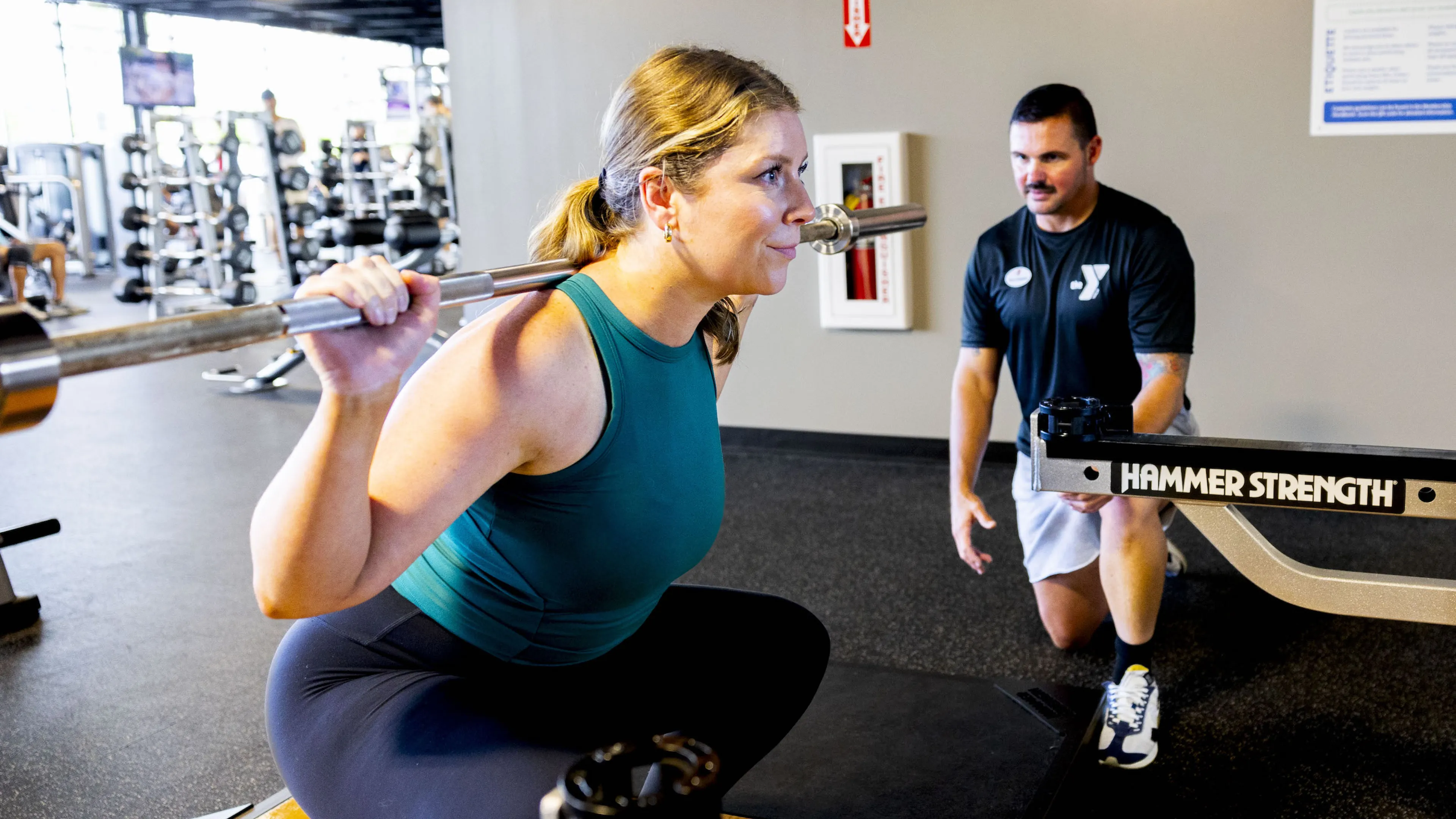 A certified YMCA Personal Trainer assists a ymca member with a deadlift squat with a plate weight bar.